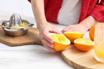 Making juice. Woman with squeezed orange at white marble table indoors, closeup