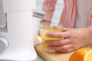 Woman making fresh orange juice with modern juicer at table indoors, closeup