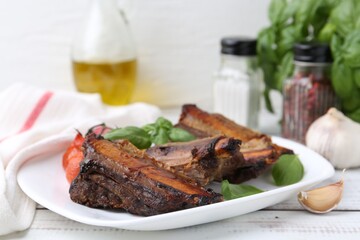 Roasted beef ribs, tomatoes and spices on white wooden table, closeup