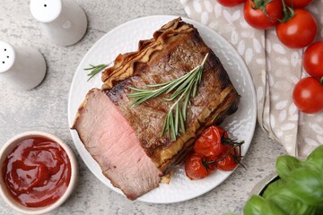 Delicious baked beef meat, tomatoes, basil, rosemary and sauce on grey table, flat lay