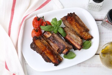 Roasted beef ribs, tomatoes and spices on white wooden table, flat lay