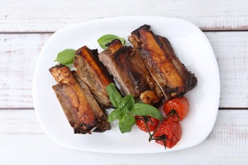 Roasted beef ribs, tomatoes and basil on white wooden table, top view