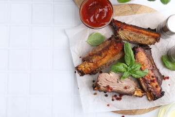 Roasted beef ribs with spices and ketchup on white tiled table, top view. Space for text