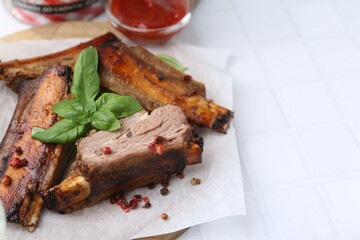 Roasted beef ribs with spices and ketchup on white tiled table, closeup. Space for text