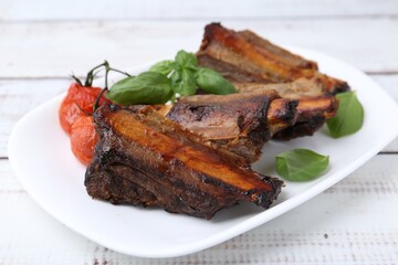 Roasted beef ribs, tomatoes and basil on white wooden table, closeup