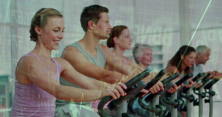 Group of six participants pedaling stationary bikes in fitness studio, with mirror reflection