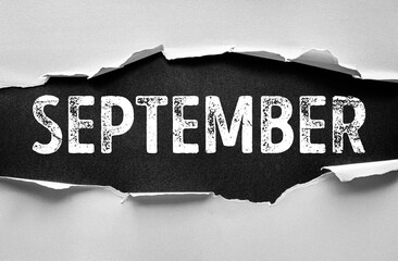 Torn paper revealing the word SEPTEMBER in bold distressed font. Concept of autumn, transitions, new beginnings, school, productivity, fresh goals, organization, and seasonal change