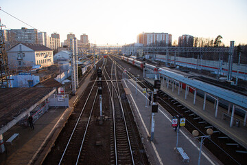 Fototapeta premium A railway station with multiple tracks and platforms. Buildings and urban structures are visible in the background. The scene is illuminated by sunset light.