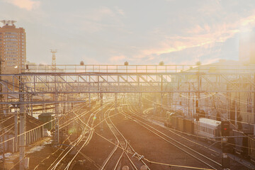 Fototapeta premium Urban railway scene at sunset with multiple tracks and buildings in the background. Soft light creates a warm atmosphere.