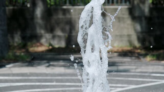 吹きあがる公園の噴水の水しぶき　夏の街の風景　暑い日差しを受けて風に煽られる水滴