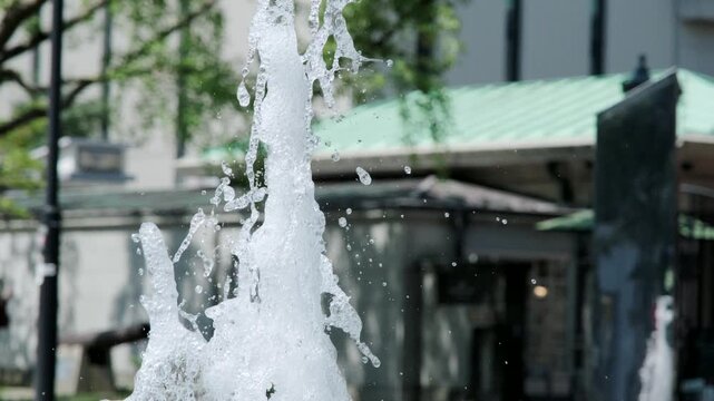 吹きあがる公園の噴水の水しぶき　夏の街の風景　暑い日差しを受けて風に煽られる水滴