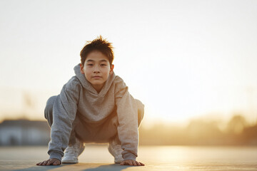 Contemplative young boy in sportswear squats outdoors against warm light. Represents determination, focus, wellness. Ideal for youth, fitness, lifestyle content.