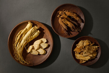 Whole ginseng roots placed in a wooden bowl next to other herbs. Overhead shot showcasing natural healing ingredients in traditional medicine. Top view, advertising photo