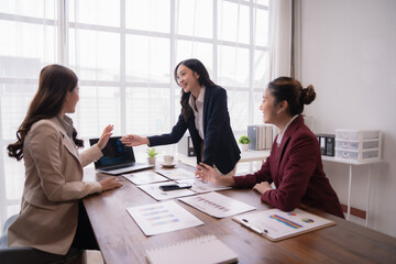 Three asian businesswomen discussing marketing strategy showing on laptop during a meeting in a modern office, pointing at the screen and smiling
