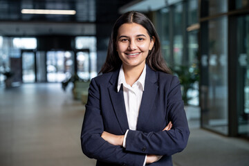 Cute young woman in jacket and white shirt standing with her arms crossed