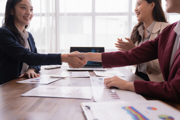 Businesswomen shaking hands after successful deal during an office meeting, celebrating their achievement together while reviewing graphs and charts on the table