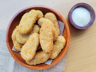 Fried chicken nuggets in a wooden plate and mayonnaise sauce in a small wooden bowl on the table.