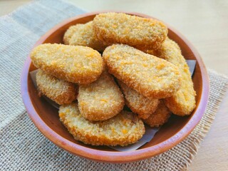 Close-up of fried chicken nuggets in a wooden plate are on the table. 