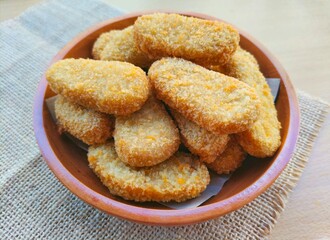 Close-up of fried chicken nuggets in a wooden plate are on the table. 