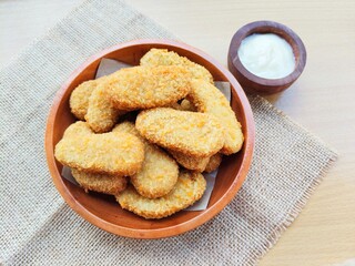 Fried chicken nuggets in a wooden plate and mayonnaise sauce in a small wooden bowl on the table.