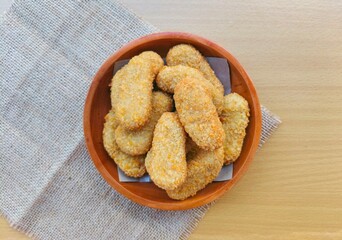 Fried chicken nuggets in a wooden plate are on the table. Top of view. 