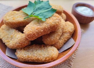 Fried chicken nuggets in a wooden plate and mayonnaise sauce in a small wooden bowl on the table.