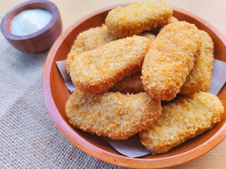 Fried chicken nuggets in a wooden plate and mayonnaise sauce in a small wooden bowl on the table.