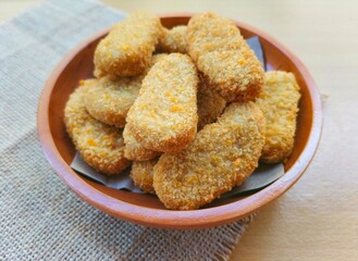 Fried chicken nuggets in a wooden plate are on the table.
