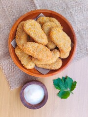 Fried chicken nuggets in a wooden plate and mayonnaise sauce in a small wooden bowl on the table.