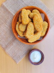 Fried chicken nuggets in a wooden plate and mayonnaise sauce in a small wooden bowl on the table.