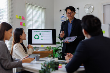 Asian businessman lead young group of multiethnic businesspeople in team meeting, using desktop computer for ESG topic presentation on monitor. Sustainable business practice, people work at office con