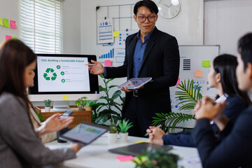 Asian businessman lead young group of multiethnic businesspeople in team meeting, using desktop computer for ESG topic presentation on monitor. Sustainable business practice, people work at office con