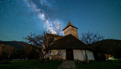 Fototapeta premium A rustic church stands under a night sky filled with stars and the milky way, creating a serene and peaceful scene.