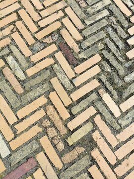 Multi color paving bricks laid in a diagonal herringbone pattern with broken weathered surface