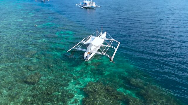 Aerial shot of traditional Philippine outrigger boats floating on clear turquoise water, with coral reefs visible below, Moalboal, Cebu, Philippines.