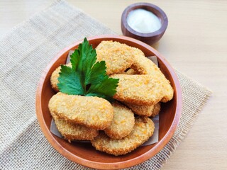 Fried chicken nuggets in a wooden plate and mayonnaise sauce in a small wooden bowl on the table.