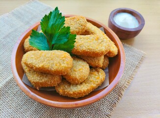 Fried chicken nuggets in a wooden plate and mayonnaise sauce in a small wooden bowl on the table.