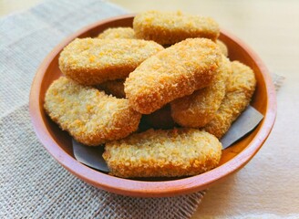 Fried chicken nuggets in a wooden plate are on the table.