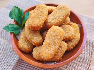 Fried chicken nuggets in a wooden plate are on the table.