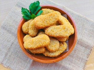 Fried chicken nuggets in a wooden plate are on the table.