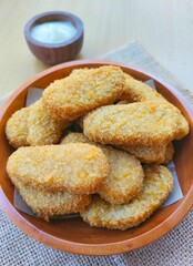 Fried chicken nuggets in a wooden plate and mayonnaise sauce in a small wooden bowl on the table.