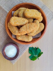 Fried chicken nuggets in a wooden plate and mayonnaise sauce in a small wooden bowl on the table.
