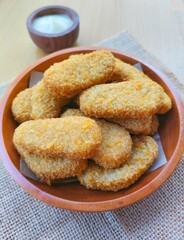 Fried chicken nuggets in a wooden plate and mayonnaise sauce in a small wooden bowl on a wooden table.