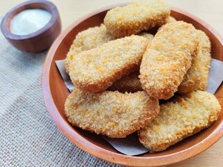 Fried chicken nuggets in a wooden plate and mayonnaise sauce in a small wooden bowl on a wooden table.
