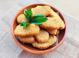 Fried chicken nuggets in a wooden plate on a wooden table. 