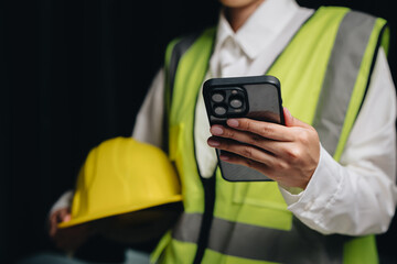 Construction Worker in Safety Vest Using Smartphone, Holding Yellow Hard Hat, Close-Up Studio Shot