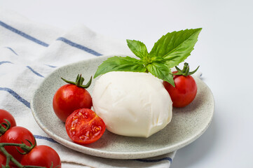 Fresh mozzarella cheese, cherry tomatoes and basil on plates on light background. Concept of Italian cuisine, capise salad and healthy eating.