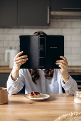 Young woman reading her Bible while having breakfast in a cozy home kitchen.
