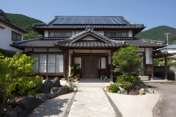 Fototapeta premium Japanese home in Okayama with black tiled roof and solar panels, front gravel yard.