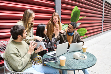Happy young multiethnic students celebrating success with high five outdoors